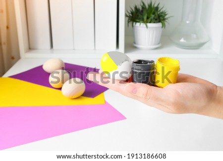 Painting Easter eggs in the trending color of 2021-yellow and gray. Egg decorated with paint, preparing for the celebration of Easter.