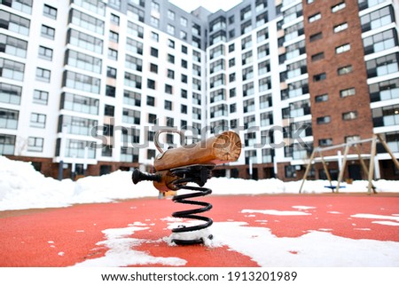 Children's attraction with springs on playground in an empty winter yard. Residential apartment building in background. Bad weather for outdoor games.