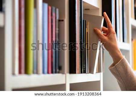 hand of woman searching for a book on shelf Royalty-Free Stock Photo #1913208364