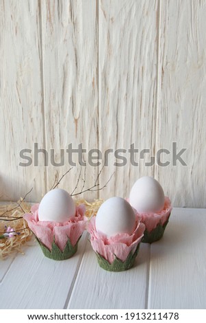 Festive spring decor, three easter eggs in flower stands on a white wooden background with natural elements