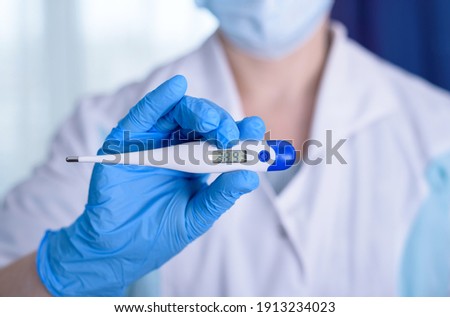 Hand in blue glove holding a digital thermometer on white background. Medical worker wearing protective gloves checking medical thermometer.