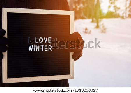 A frame with the inscription I love winter in the hands of a woman in gloves in nature, toned photo.