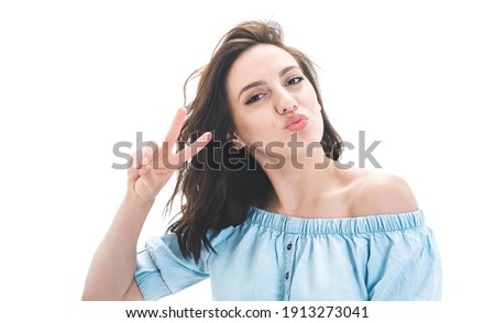 Pretty girl shows peace sing with fingers and send kiss to you, isolated on white background. Joyous lovely woman kissing. Studio shot