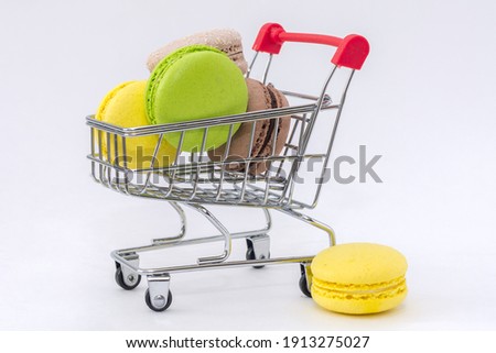 A close-up on a white background is a supermarket cart filled with delicious French sweets. Macaron. Concept - shopping in a supermarket or online store, delivery of any product to your home Royalty-Free Stock Photo #1913275027