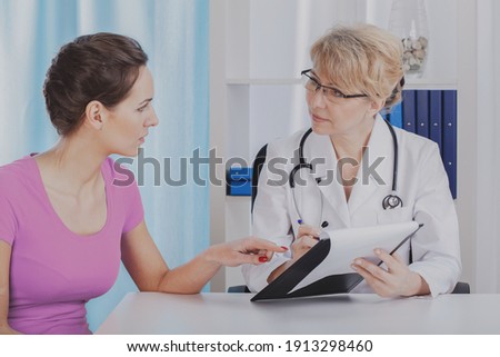 Senior female doctor showing medical records to her young beautiful patient Royalty-Free Stock Photo #1913298460