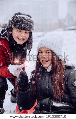two children a boy and a girl with long hair braces outside during the day at the stadium it is snowing laughing in their hands holding sparklers bright fireworks are sitting on a skating plate