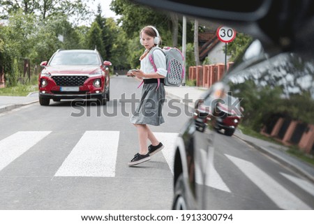 Scared girl with phone and headphones runs away from the car at a pedestrian crossing Royalty-Free Stock Photo #1913300794