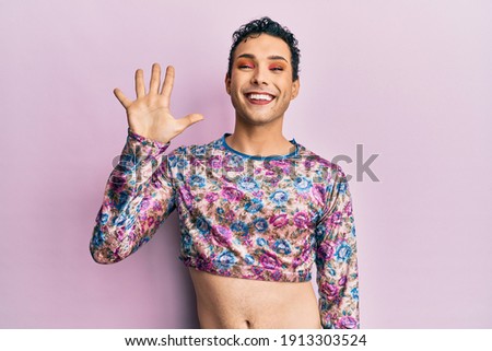 Handsome man wearing make up wearing fashion clothes showing and pointing up with fingers number five while smiling confident and happy. 