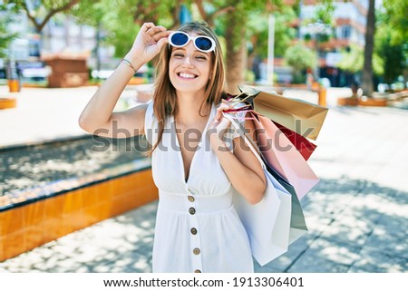 Young blonde woman smiling happy holding shopping bags at street of city