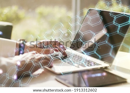 Double exposure of technology hologram with hexagon and hands typing on laptop on background. Research and development software concept
