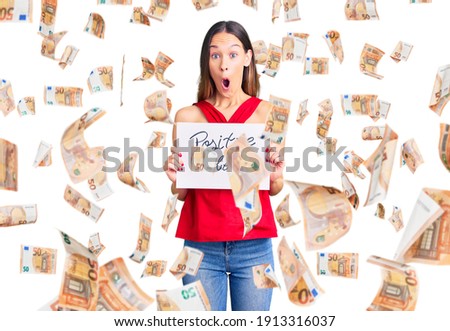 Beautiful brunette young woman holding positive vibes banner scared and amazed with open mouth for surprise, disbelief face