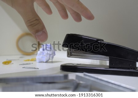 Stapler, clips and other writing materials thrown over white table while a mother of man goes against an object