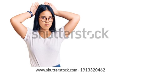 Young beautiful asian girl wearing casual clothes and glasses doing bunny ears gesture with hands palms looking cynical and skeptical. easter rabbit concept. 