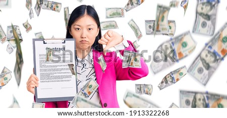 Young beautiful chinese woman holding clipboard with contract document with angry face, negative sign showing dislike with thumbs down, rejection concept