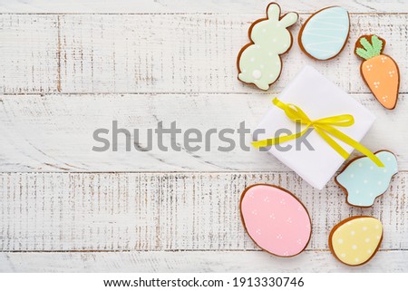 Easter greeting card with colorful rabbits, eggs, chickens and carrots gingerbread cookies on white wooden old background with copy space. Mock up. Banner. Top view.