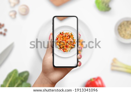 Photographing the preparation of a diet meal with vegetables with smart phone. Woman holding phone in vertical position