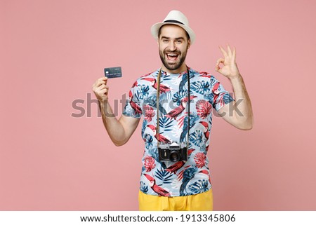 Excited young traveler tourist man in summer clothes hat hold credit bank card showing OK gesture isolated on pink background studio. Passenger traveling abroad on weekend. Air flight journey concept