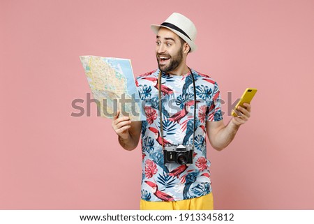 Excited young traveler tourist man in summer clothes hat using mobile cell phone hold city map isolated on pink background. Passenger traveling abroad on weekends getaway. Air flight journey concept
