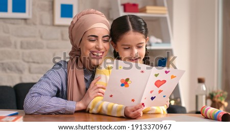 Happy Mother's Day! Beautiful little girl congratulates her mother wearing a headscarf. The girl is reading the heartfelt letter she wrote to her mother.