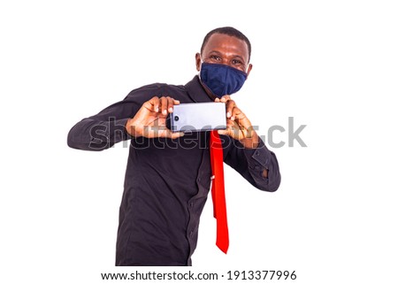portrait of a handsome young man wearing a cloth medical mask and taking picture with a mobile phone.