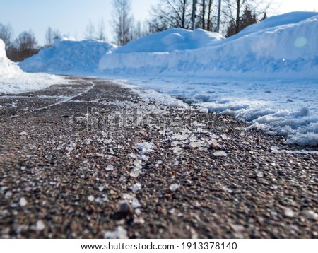 Salt grains on icy sidewalk surface in the winter. Applying salt to keep roads clear and people safe in winter weather from ice or snow, closeup view
