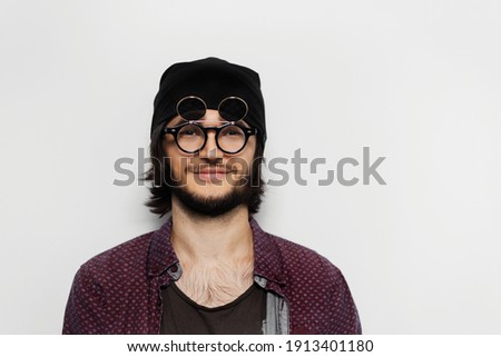 Studio portrait of smiling guy on white background. Wearing round glasses and hat.