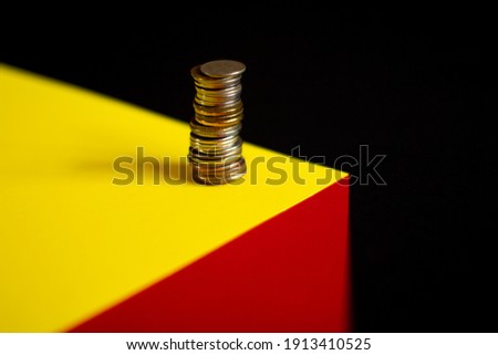 On a black background, a volumetric geometric figure on which there is a stack of coins 