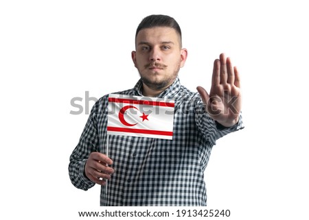 White guy holding a flag of Turkish Republic of Northern Cyprus and with a serious face shows a hand stop sign isolated on a white background.