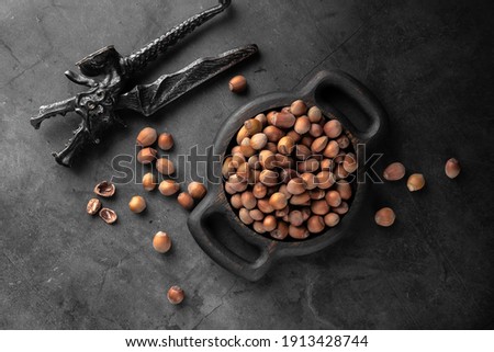 dragon shaped vintage nutcracker and many unpeeled hazelnuts on a black plate and dark background, top view