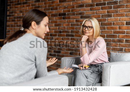 Worried young woman patient sitting at a psychologist's therapist appointment and telling about mental problems, attentive mature female doctor is listening and making notes. Psychotherapy concept Royalty-Free Stock Photo #1913432428