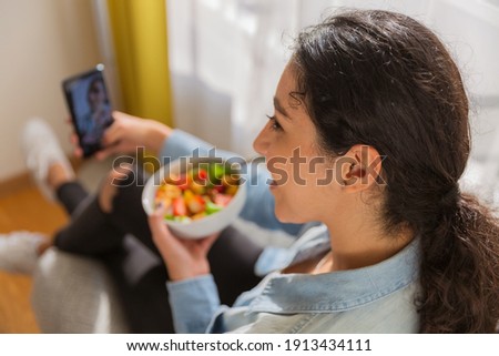 Smiling brunette young woman sitting on a chair and taking a selfie with her salad in her room