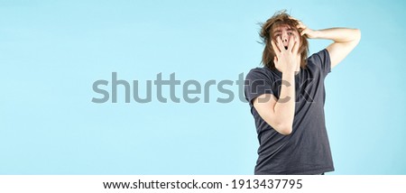 The suffering and pain of experiencing loss. An emotional young man in a T shirt shows acting gestures holding his head with his hands isolated on a blue background