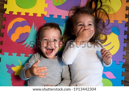 childhood, family friendship, games - close up portrait Two funny joy happy smiling little toddler peschool kids siblings twins brother with sister have fun lie laughing on puzzles mat at home indoors Royalty-Free Stock Photo #1913442304