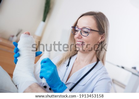 Professional smiling nurse bandages a patient's leg with a medical bandage.