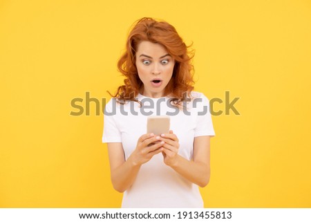 Woman surprised with smartphone. Photo of millennial girl with ginger hair uses mobile phone for sending text messages. surpised emotions, technology concept Royalty-Free Stock Photo #1913455813