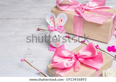 Handmade traditional Easter symbols concept. Cute rabbit from the egg, gift box, festive decor in pink tones. White wooden background, copy space