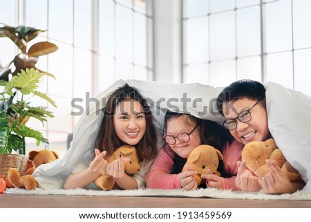 Happy Asian family laying on carpet in living room and smile with their daughter down syndrome child , Look at the camera show sign mini heart , Activity happy family lifestyle concept.