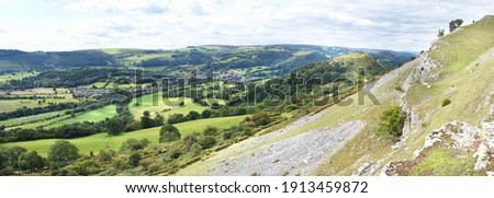 Panoramic view of the Vale of Llangollen, with the town, ruins of Castell Dinas Bran, camping sites and fields following the River Dee through the valley below the Welsh hills all within the photo. 