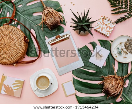 Flat lay women's office desk. Female workspace with clip board, tropical leaves, accessories, cup of coffee on pink background. Top view .Copy space