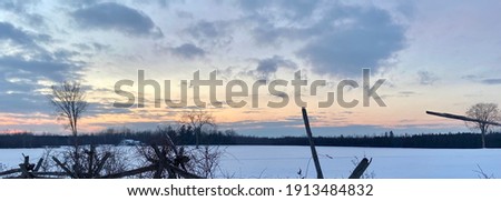 Beautiful sunset and a snow covered field and cedar fencing in foreground.