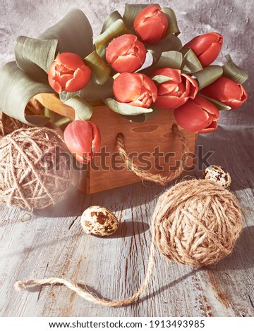 Spring or Easter celebration decor. Natural zero waste decorations. Hemp balls, bunch of red tulips, spring decorations and painted Easter eggs on gray rustic wooden table.