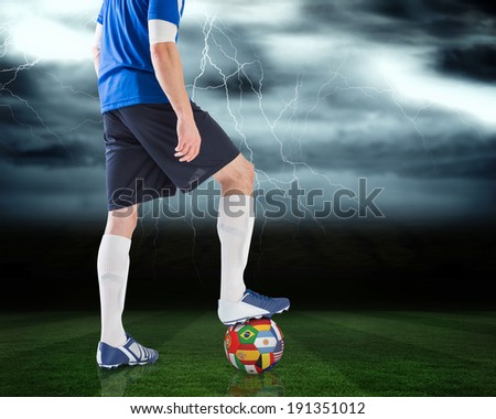 Composite image of football player standing with international ball against football pitch under stormy sky