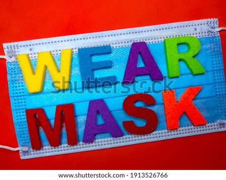 Selective focus.Word WEAR MASK on a face mask with red background.Protection concept.Shot were noise and film grain.