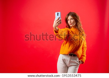 young woman on red background taking pictures of herself on mobile phone