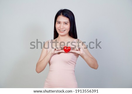 Portrait of beautiful Asian young woman holding pointing red heart shape isolated on light gray background with copy space