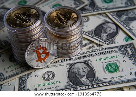 Pile of US dollar cash. Next to it are a number of gold bitcoins and a silver digital cryptocurrency coin. Bank image and commercial photo background. 