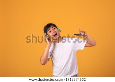 Happy young Asian man wearing headphones on orange background.