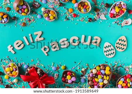 Easter frame with chocolate eggs and sweets on a turquoise, green, blue background. Feliz Pascua - happy easter text in Spanish. Top view, flat lay