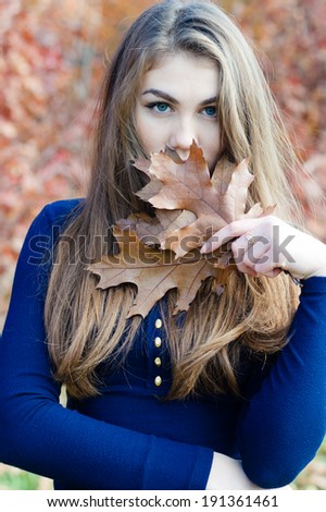 Picture of closeup portrait of beautiful woman hiding face behind autumn brown leaf outdoors background