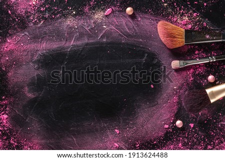 Makeup background with brushes, pearls, and crushed cosmetics, overhead flat lay shot on a dark background